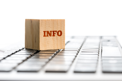 Red Info Text on Small Wooden Block Above Computer Keyboard. Isolated on White Background.
